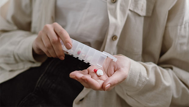 person-pouring-pills-into-their-hand-from-a-pill-organizer