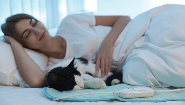 woman and cat in bed with heating pad