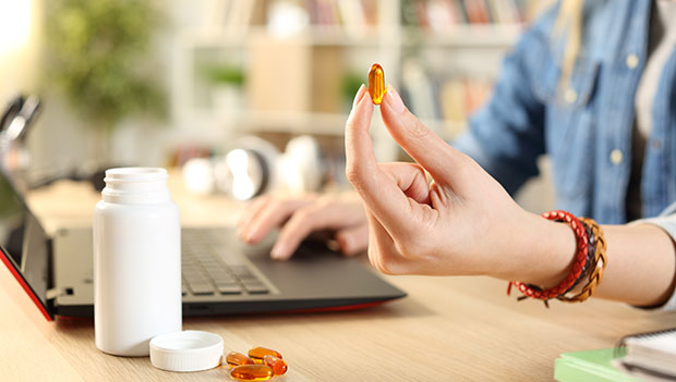 teen holding multivitamin while on computer