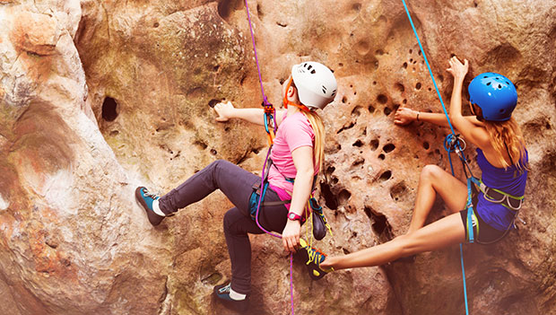 two climbers wearing harnesses climbing a rock
